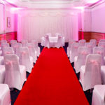 The Park Lane Suite at Mercure York Fairfield Manor Hotel, set up for a wedding ceremony, red carpet aisle, pink lighting