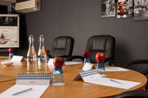 Meeting table at Mercure London Watford, black leather office chairs around a wooden table with glasses of water and apples